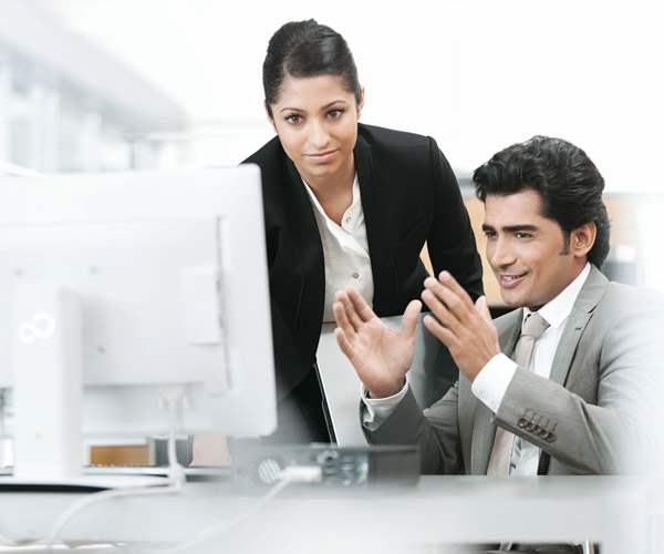 Two people study a computer screen, one is gesturing as-if making a point to the other